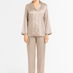 Woman wearing a beige silk pajama set with ivory piping details on a white background
