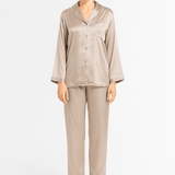 Woman wearing a beige silk pajama set with ivory piping details on a white background