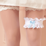 Model wearing white lace garter with light blue bow, from The Foundation, a perfect “something blue” under a wedding dress for a classic bridal touch.