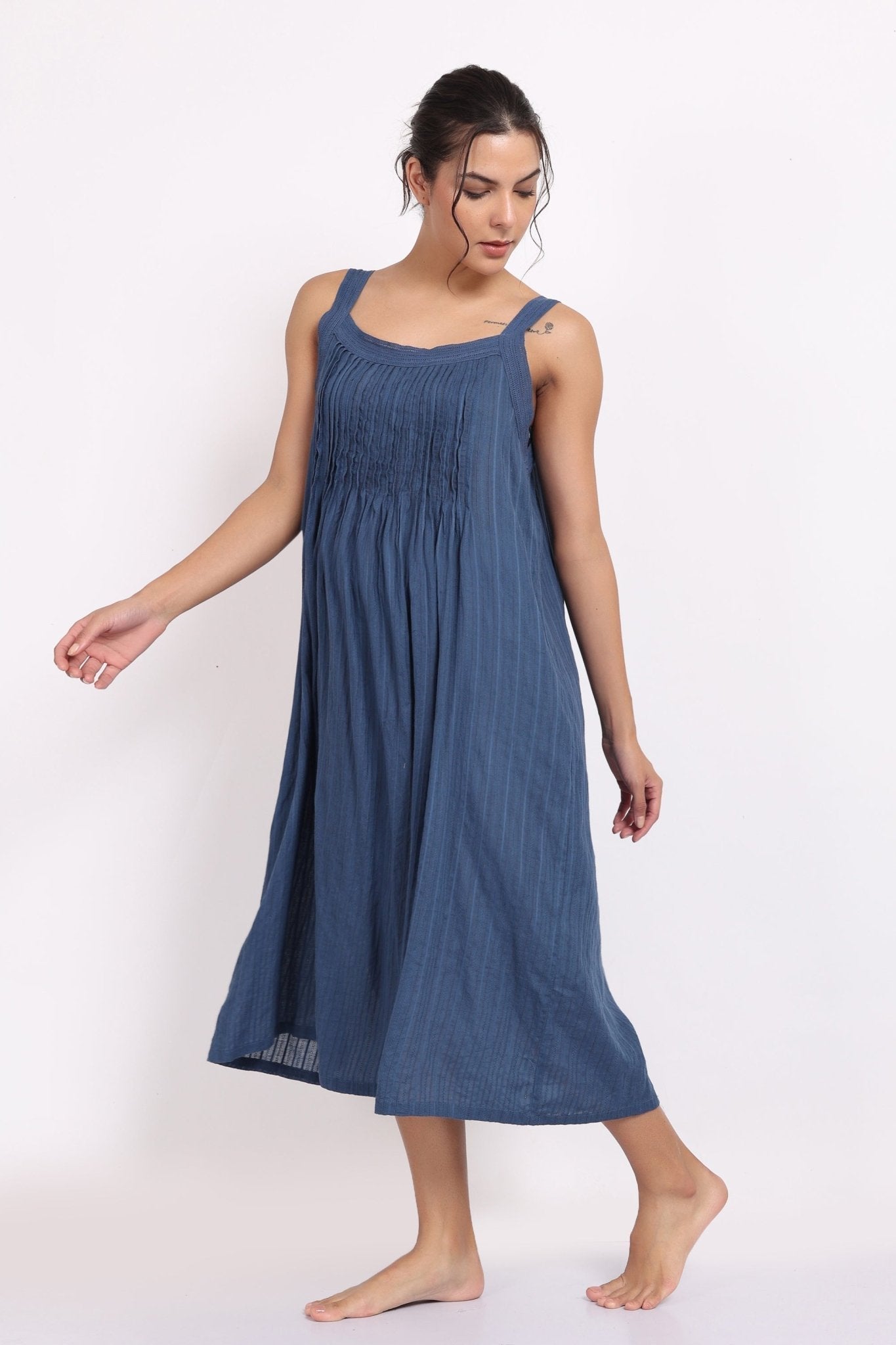 Woman wearing a sleeveless blue cotton nightie with pintuck detailing and a relaxed flowing fit.