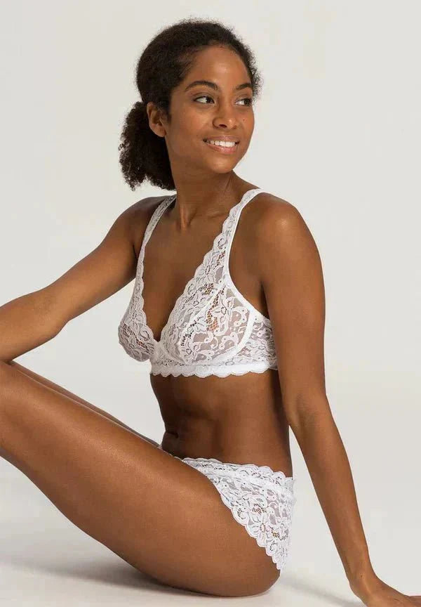 Model wearing Hanro Moments Soft Cup Bra and Briefs in White lace, seated against a neutral background