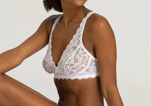 Model wearing Hanro Moments Soft Cup Bra and Briefs in White lace, seated against a neutral background