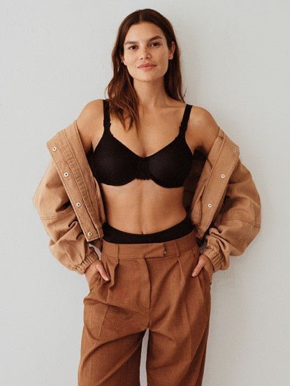 Woman wearing Chantelle Hedona Minimiser Bra in black with high-waisted brown trousers and a tan jacket.