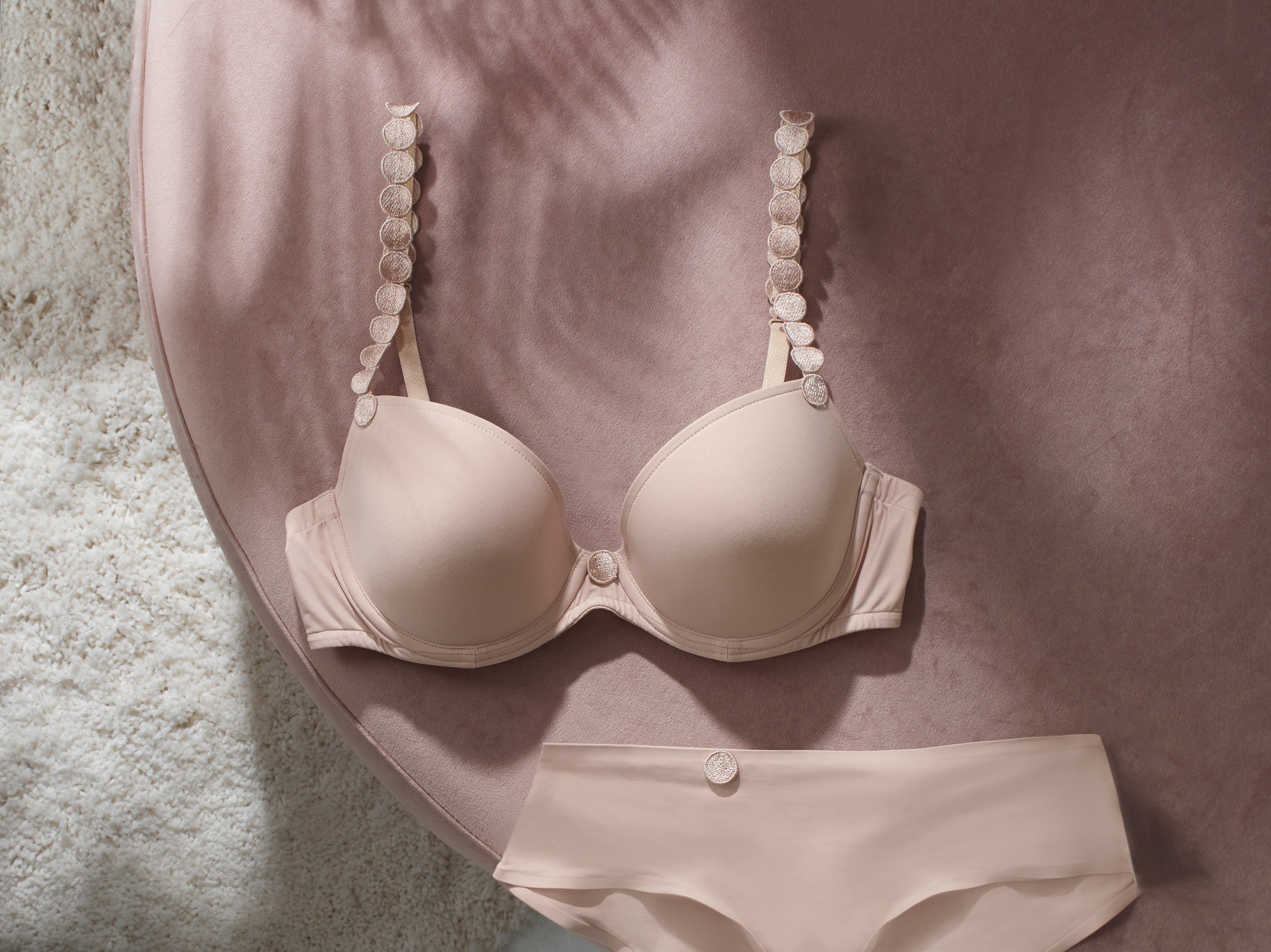 Marie Jo Tom Padded Heart Shaped Convertible Bra in Cafe Latte with matching briefs, laid flat on a blush upholstered chair.