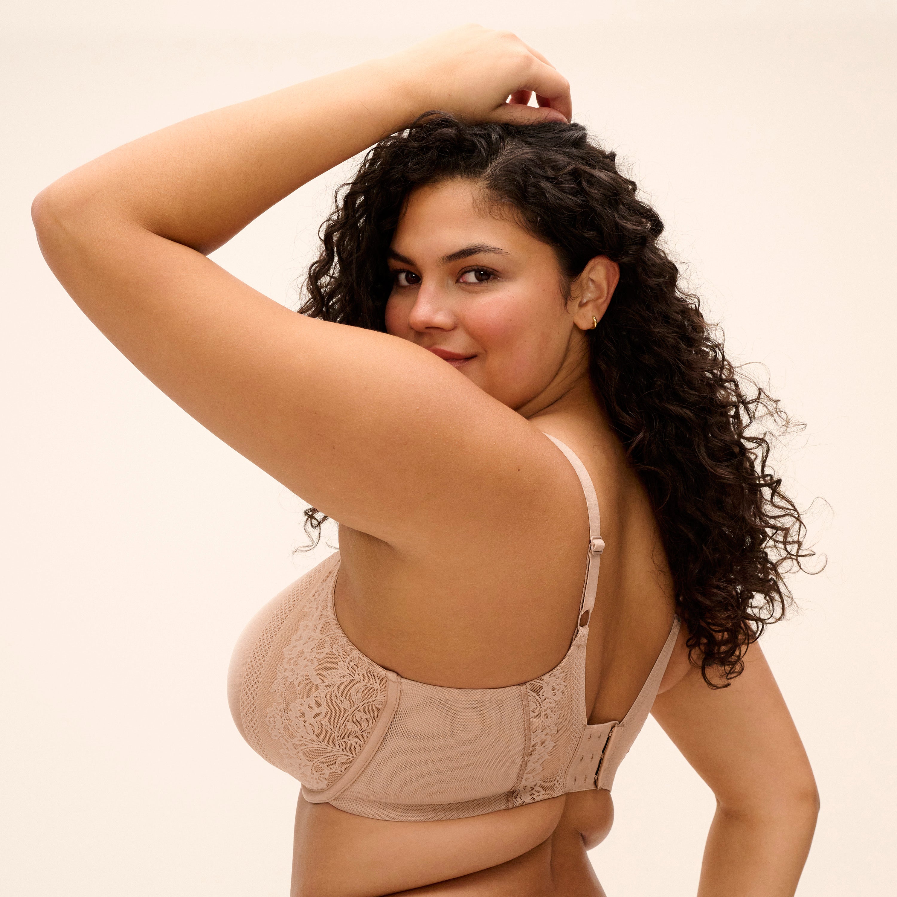 Woman wearing a nude lace full coverage bra with adjustable straps, shown from the back with curly hair against a neutral background.