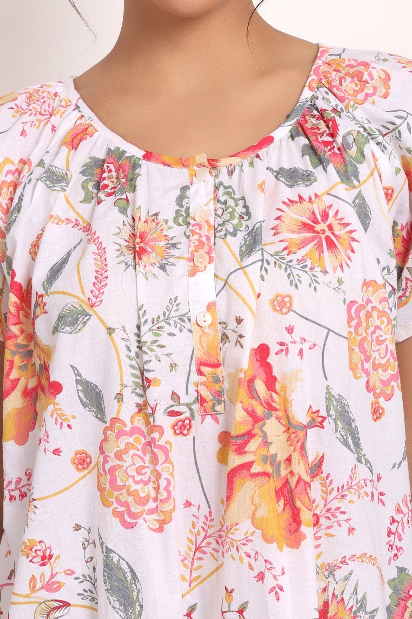 Detailed view of buttoned neckline with softly gathered pleats and coral floral print.