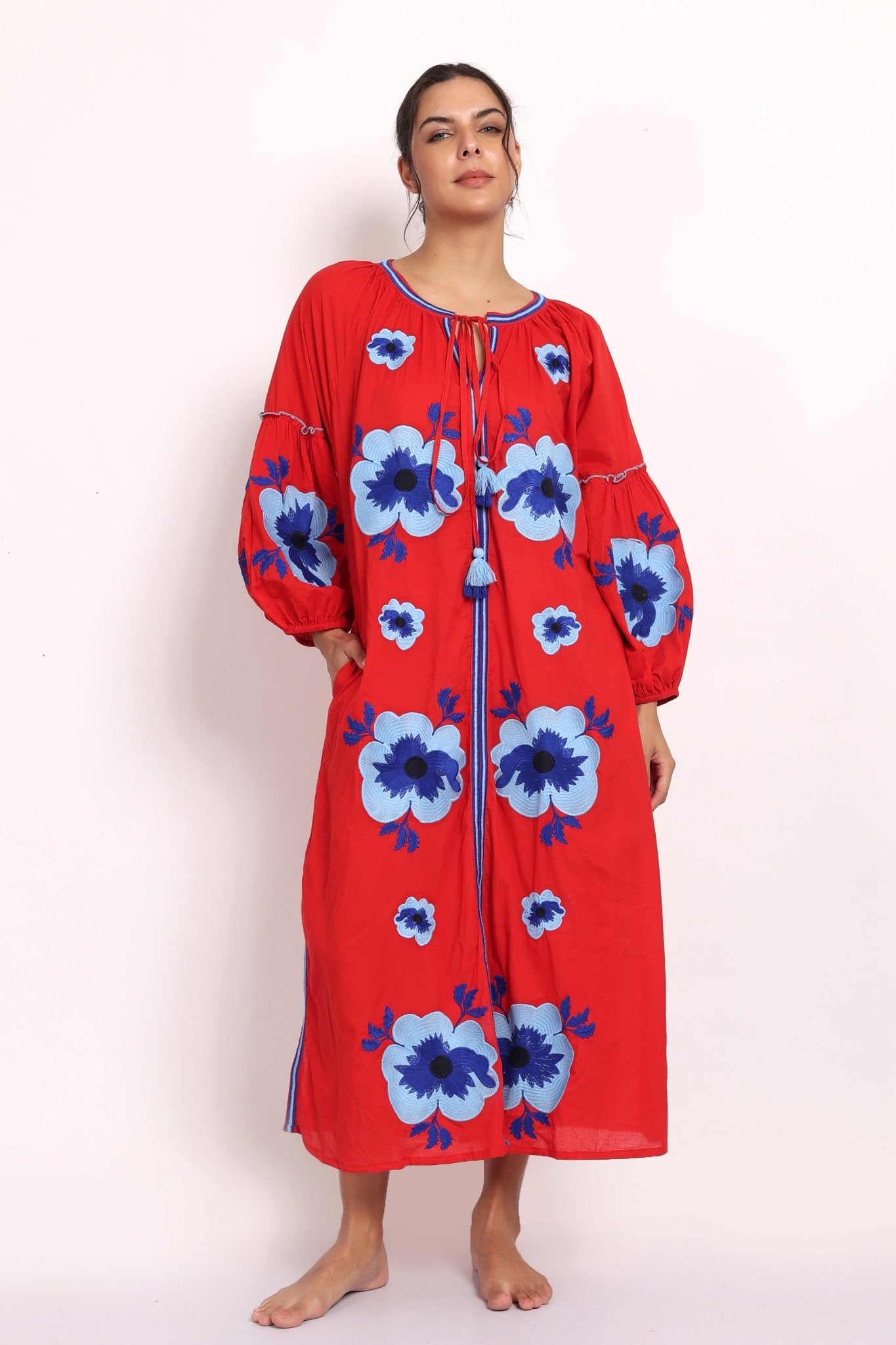 Model in bright red cotton sundress with bold blue floral embroidery, front view.