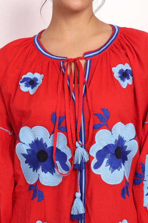 Close-up of v-neckline and tassel tie on red Romani cotton sundress with floral embroidery.