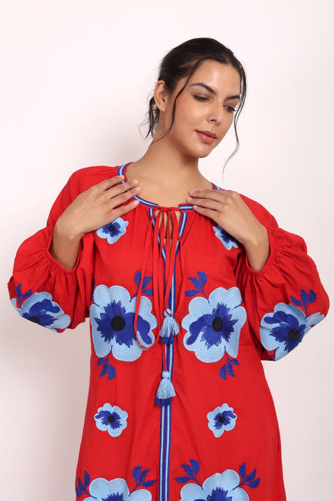 Model smiling in red embroidered sundress showing soft neckline and relaxed drape.