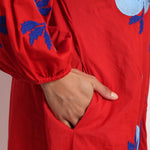 Close-up of blue floral embroidery on red cotton fabric sleeve.