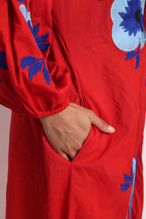 Close-up of blue floral embroidery on red cotton fabric sleeve.