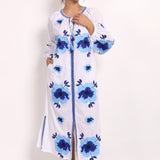Model wearing white cotton sundress with navy floral embroidery, front view, arm raised.