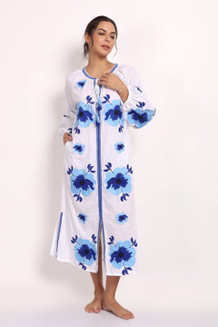 Model wearing white cotton sundress with navy floral embroidery, front view, arm raised.