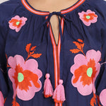 Detailed shot of pink floral embroidery and tassel neckline on navy cotton dress.