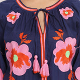 Detailed shot of pink floral embroidery and tassel neckline on navy cotton dress.