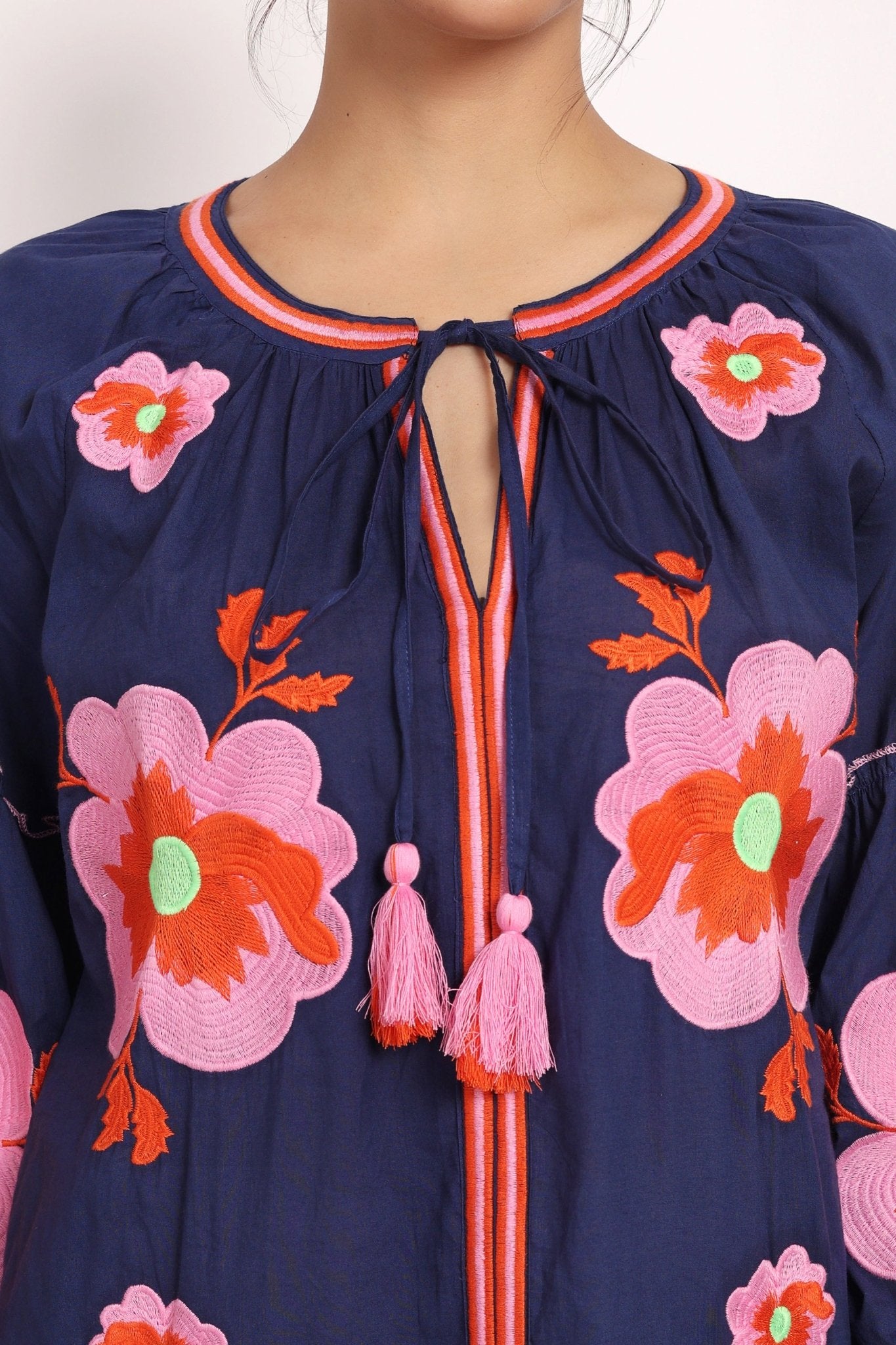 Detailed shot of pink floral embroidery and tassel neckline on navy cotton dress.