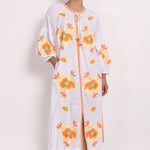 Model wearing white cotton sundress with beige floral embroidery, front view with tassel tie neckline.