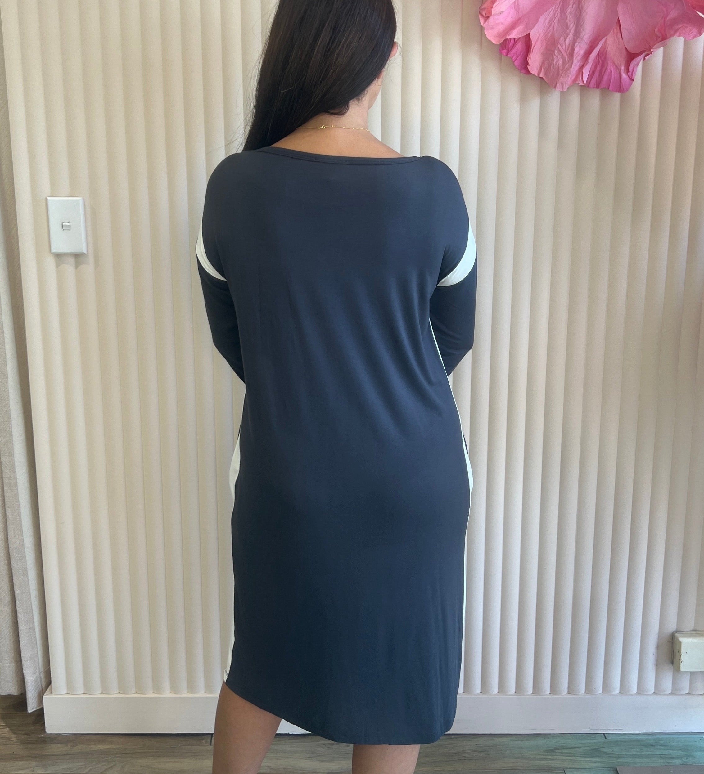 Person wearing a dark blue dress standing in front of a decorative wall with large pink flowers.