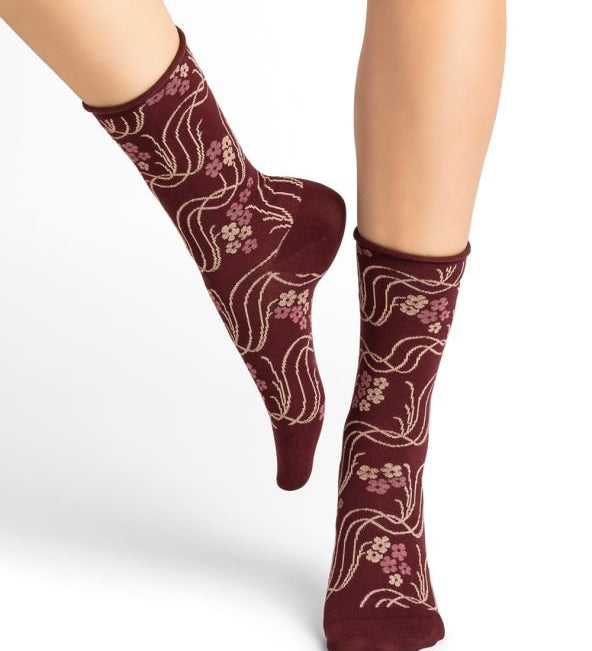 Model wearing Bleuforet Velvet Cotton Wild Flowers Mid Socks in Chianti, featuring a wild flower print and glittery threads, available at The Foundation.