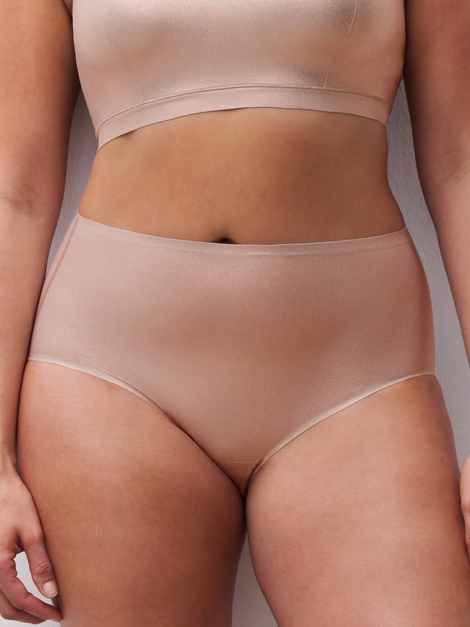 Woman wearing a beige bra and panties set against a plain background