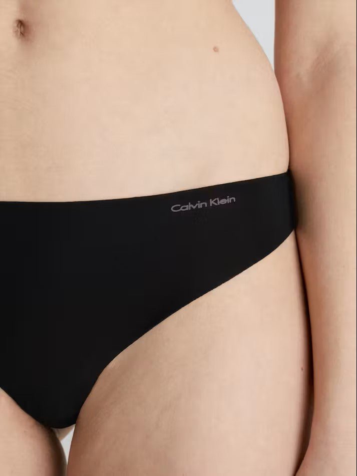 Side angle of Calvin Klein Invisibles Thong Black, highlighting the medium rise waist and logo detail on waistband.