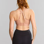 Woman wearing a beige sports bra and black leggings on a gray background