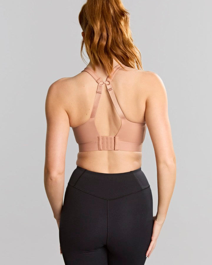 Woman wearing a beige sports bra and black leggings on a gray background