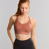 Woman wearing a brown sports bra and black leggings on a gray background