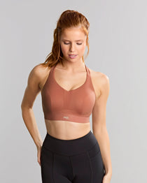 Woman wearing a brown sports bra and black leggings on a gray background