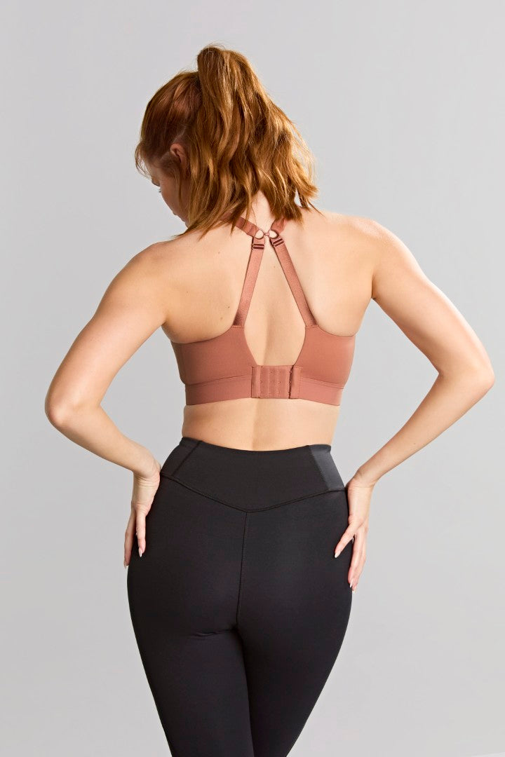 Woman wearing a brown sports bra and black leggings on a gray background