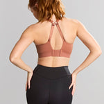 Woman wearing a brown sports bra and black leggings on a gray background