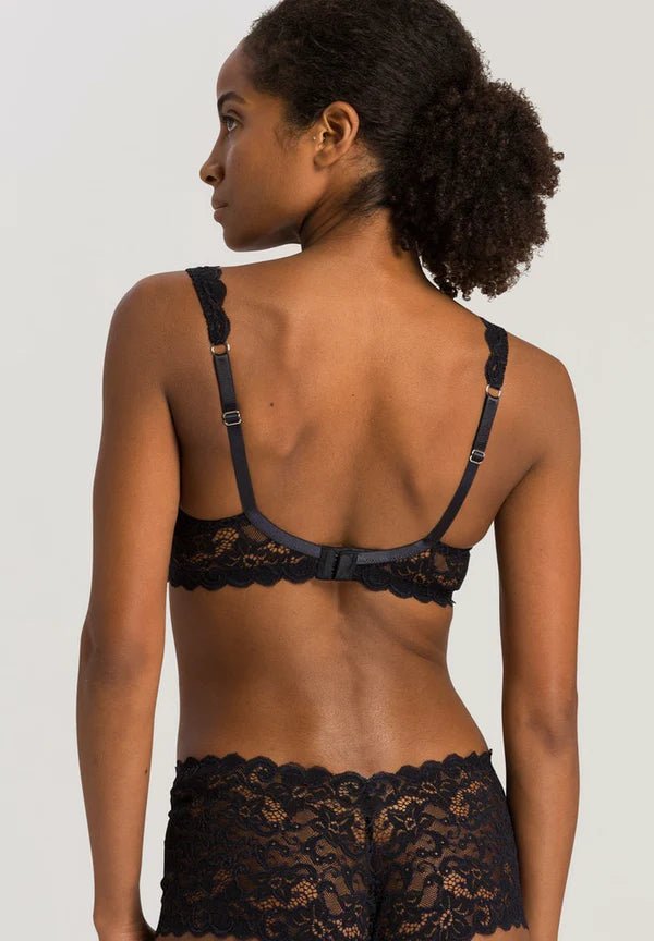 Woman wearing a black lace bra and panties set against a plain background