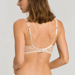 Back view of a woman wearing a beige lace bra and panties set against a plain background