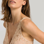 Close up view of a woman wearing a beige lace bralette against a plain background