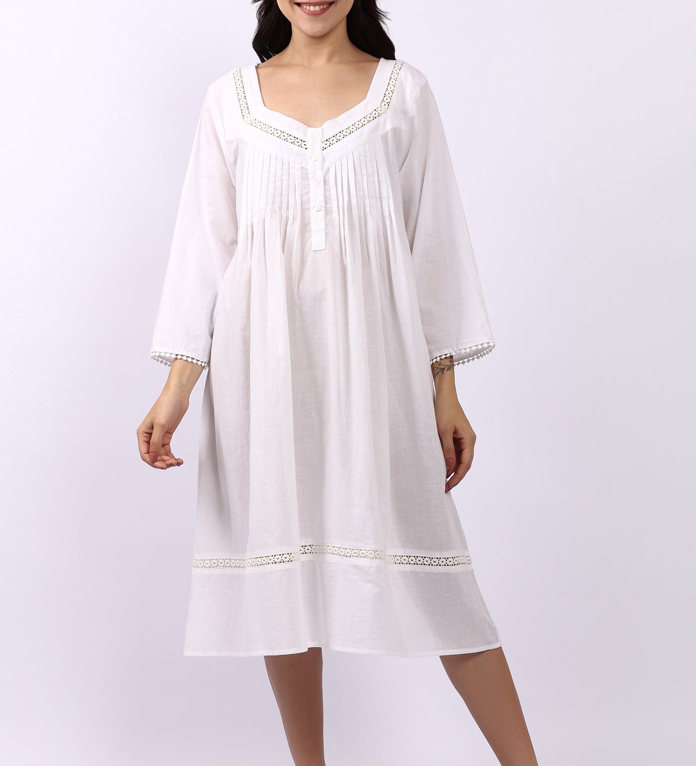 Woman wearing Lotus Susie white cotton nightdress with 3/4 sleeves, lace trim and pintuck bodice.