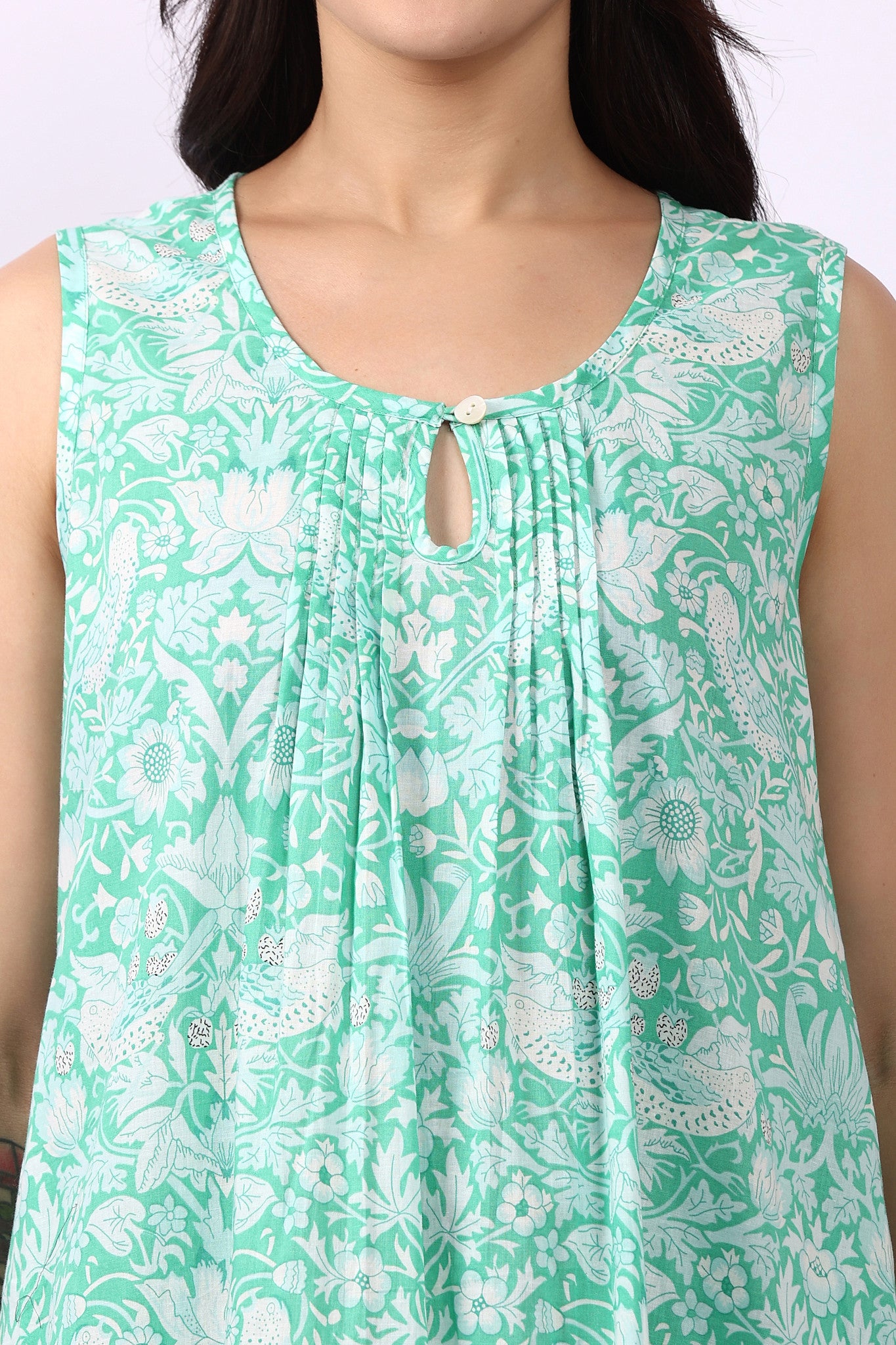 Woman wearing sleeveless cotton nightdress in spearmint green with Strawberry Thief print, keyhole neckline, and relaxed fit close up of pin tuck details.