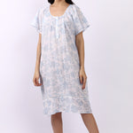 Woman wearing white cotton nightdress with sky-blue floral print and cap sleeves, button neckline.