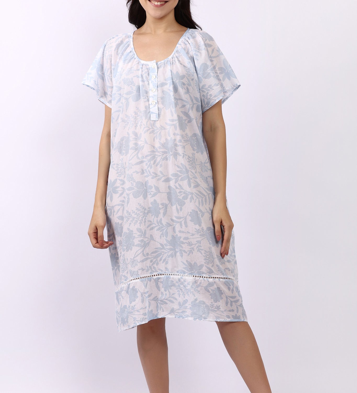 Woman wearing white cotton nightdress with sky-blue floral print and cap sleeves, button neckline.