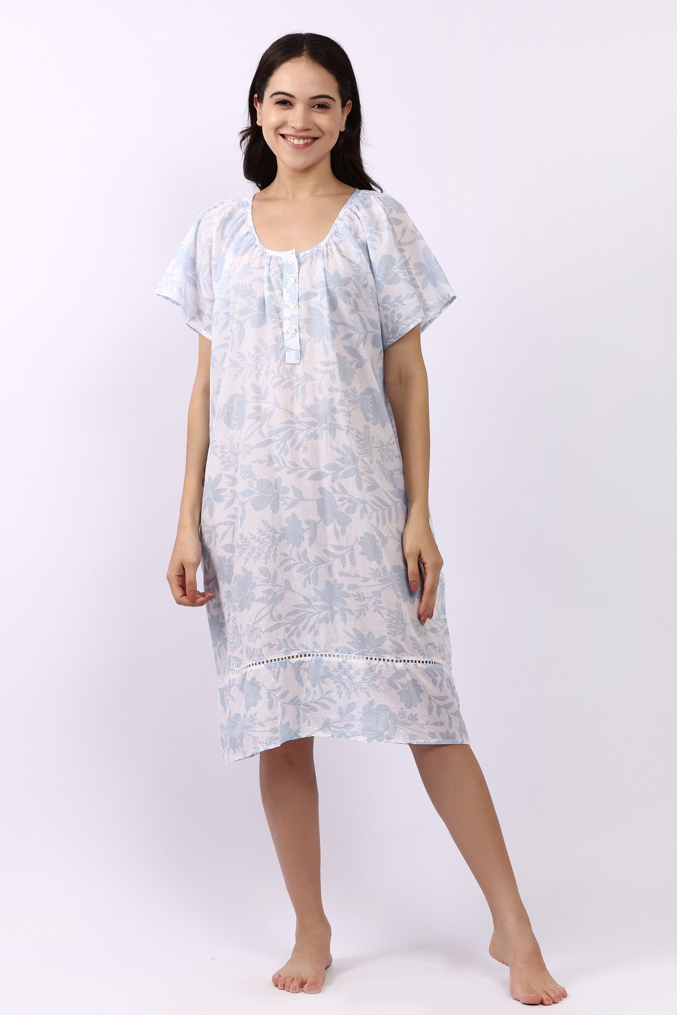 Woman wearing white cotton nightdress with sky-blue floral print and cap sleeves, button neckline.