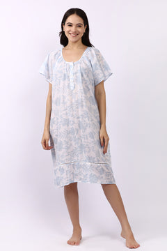 Woman wearing white cotton nightdress with sky-blue floral print and cap sleeves, button neckline.