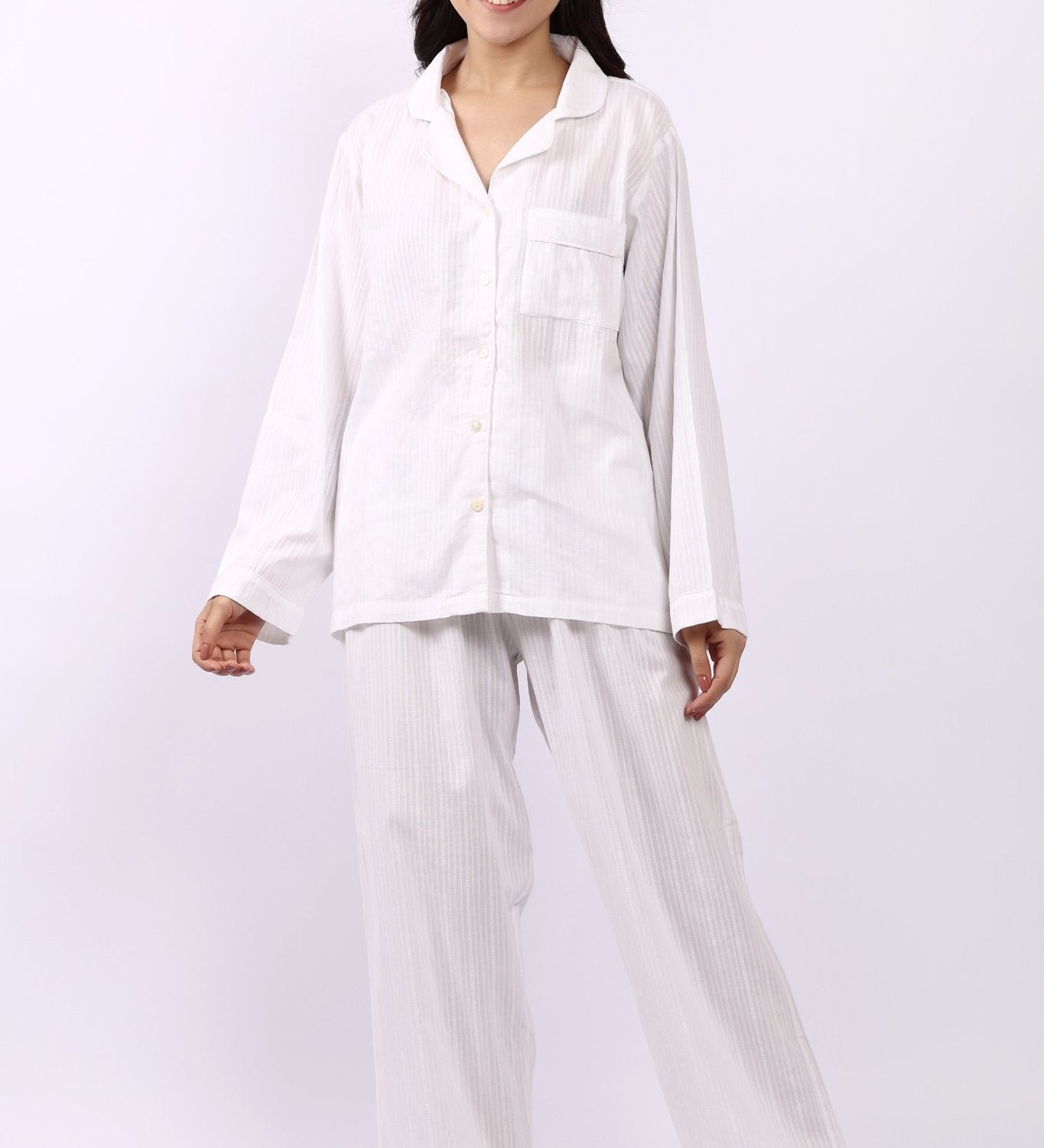 Woman wearing Lotus Jacqui revere long pyjama set in white self-stripe cotton, shirt and pants.