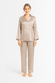Woman wearing a beige silk pajama set with ivory piping details on a white background