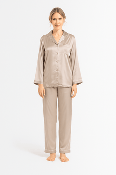Woman wearing a beige silk pajama set with ivory piping details on a white background