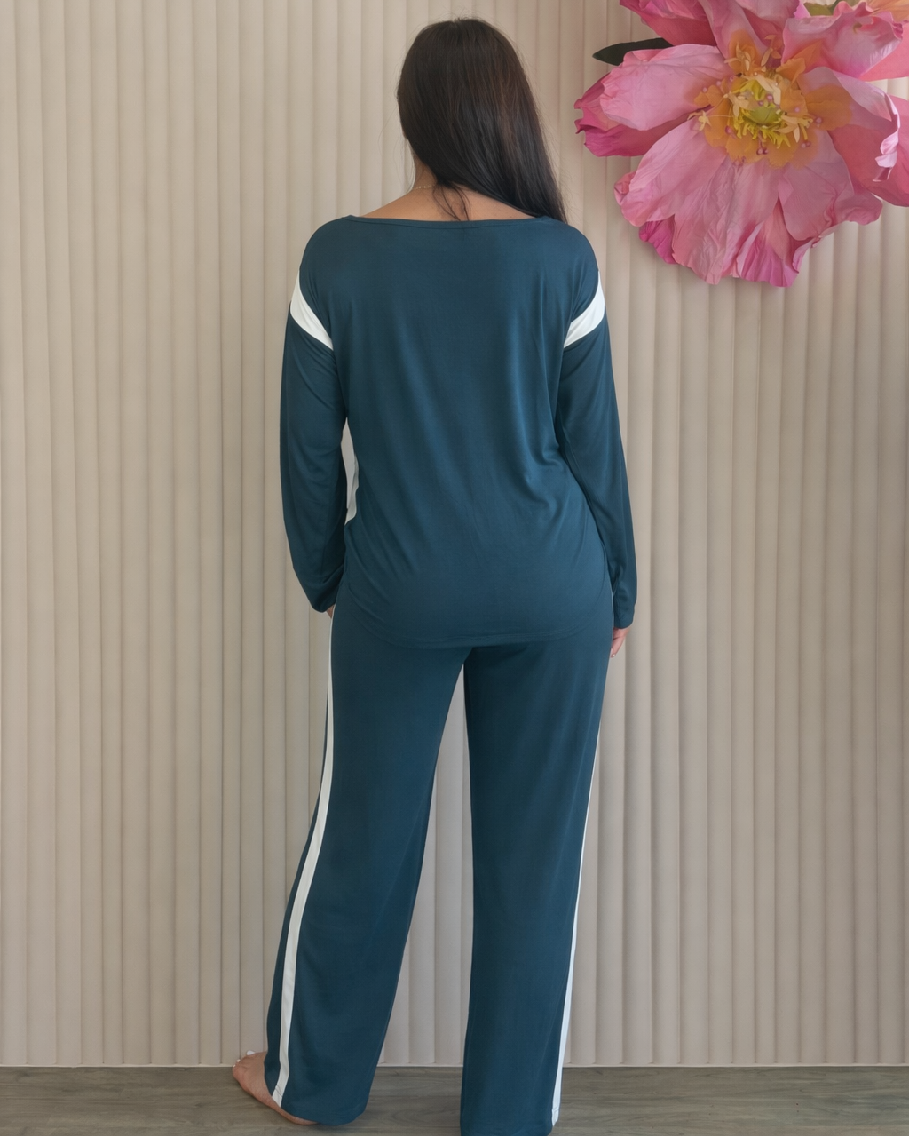 Woman wearing a teal outfit with white stripes standing in front of a floral arrangement.