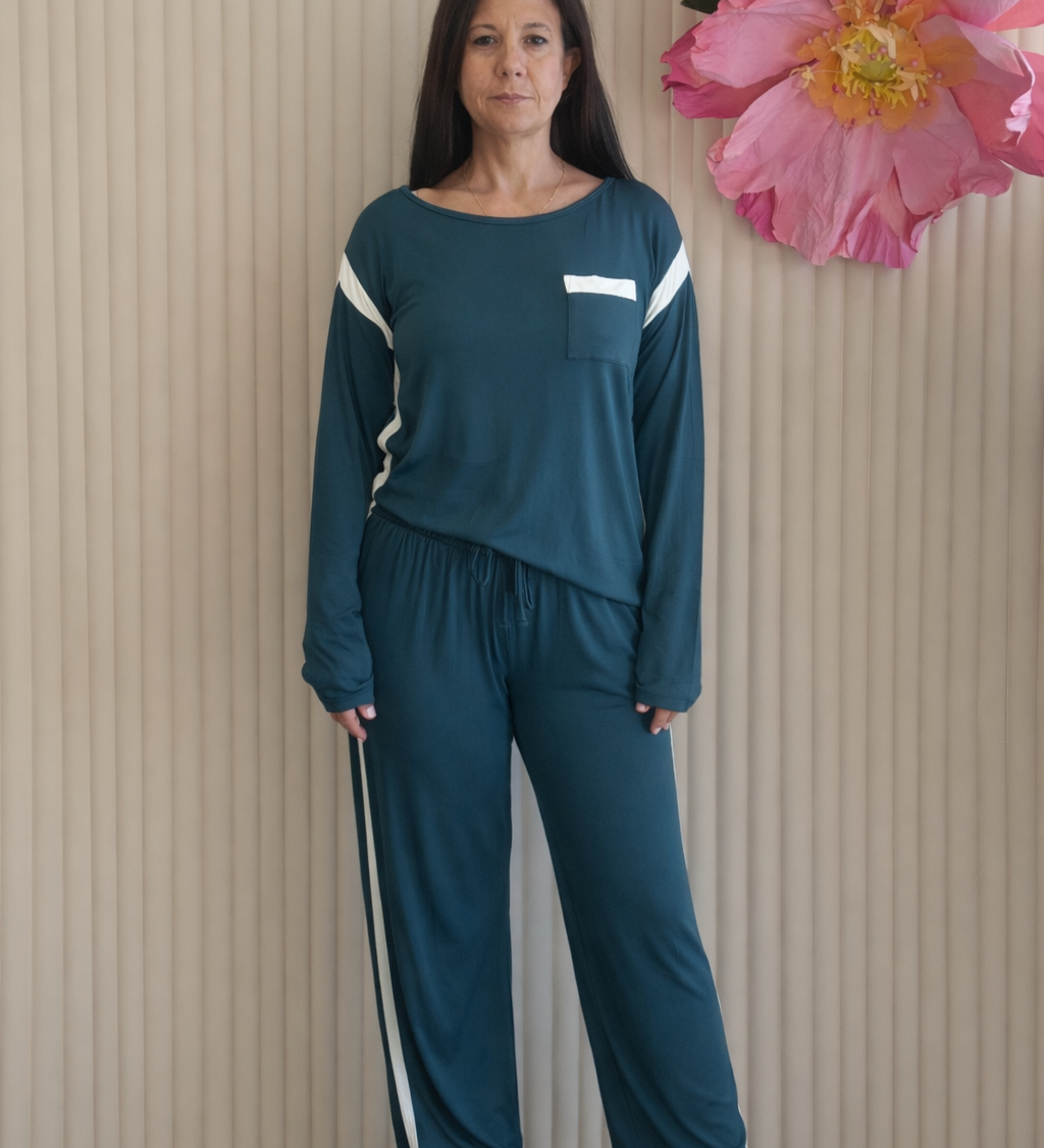 Woman wearing a teal tracksuit standing in front of a beige wall with decorative flowers.