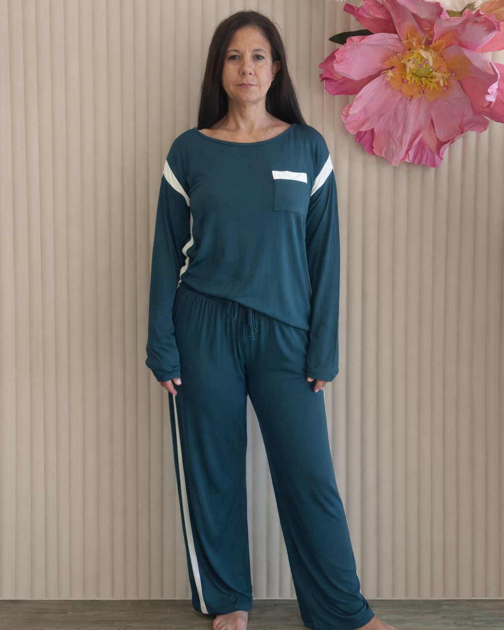 Woman wearing a teal tracksuit standing in front of a beige wall with decorative flowers.