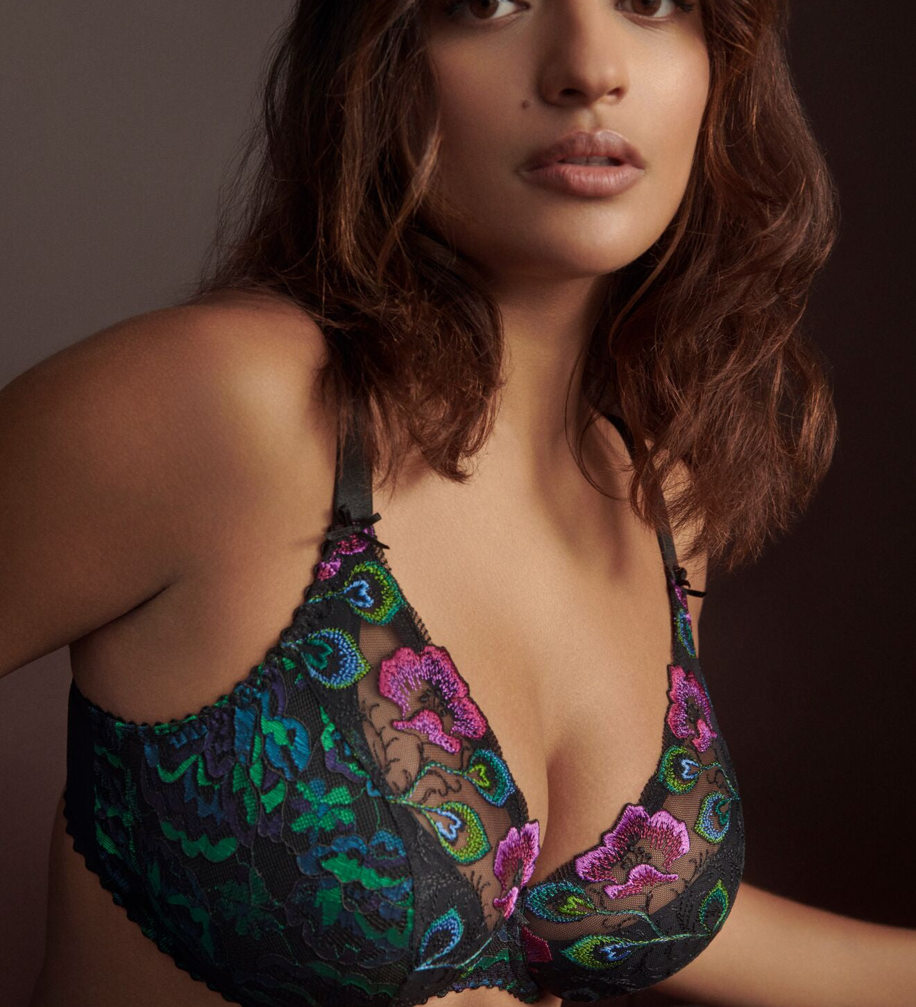 Confident woman in Prima Donna San Angel Half Padded Plunge Bra Peacock Feather, peacock blues and greens glowing against black, styled by The Foundation.