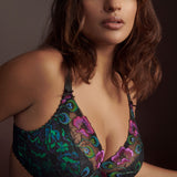 Confident woman in Prima Donna San Angel Half Padded Plunge Bra Peacock Feather, peacock blues and greens glowing against black, styled by The Foundation.