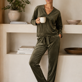 Woman in olive green pajama set holding a mug in a minimalistic room.