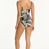 Woman wearing a black and white leaf print swimsuit on a black background back view